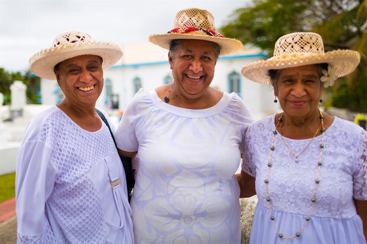 Three Cook Islands women in white dresses and woven hats