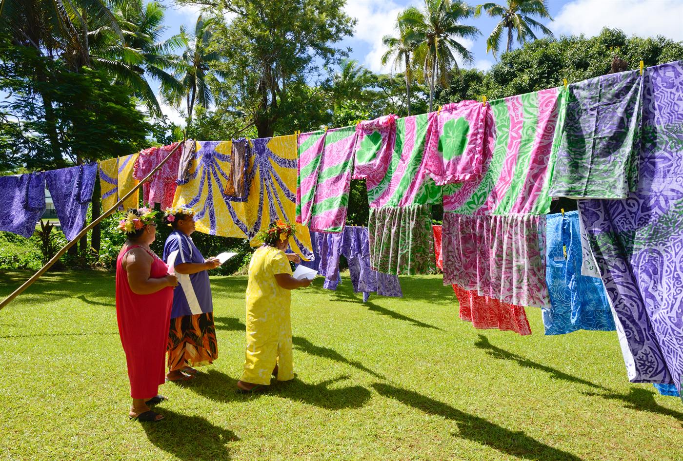 Women judging colourful tivaevae quilts hung outdoors on Enuamanu (Atiu)